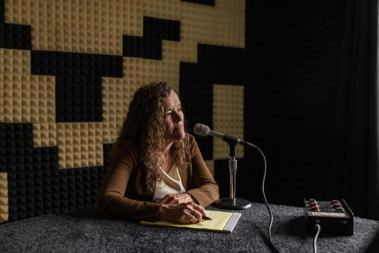 Anne Hallward sits in a radio recording studio in front of a mircophone