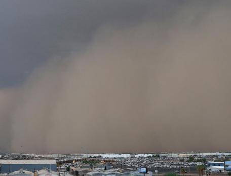 Dust storm rolling in over landscape dotted with small buildings