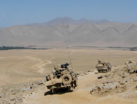 Military vehicles traveling over desert terrain with mountains in the distance