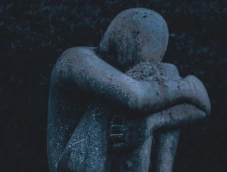 detail of a sculpture of a figure seated with knees pulled to chest