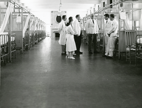Image of mid-century photo, William Bosworth Castle, MD 1921 (center) talks with medical staff and faculty in a ward at Boston City Hospital