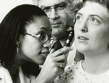 medical student examines the inner ear of a patient as a clinican looks on