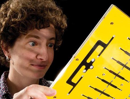 woman looking at yellow piece of plastic with cutouts