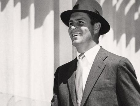 black and white photo of a smiling suited man wearing a fedora