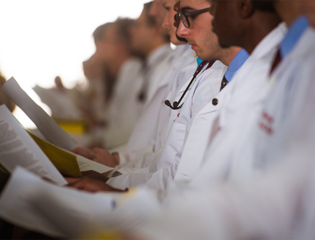 Students in white coats read paper documents