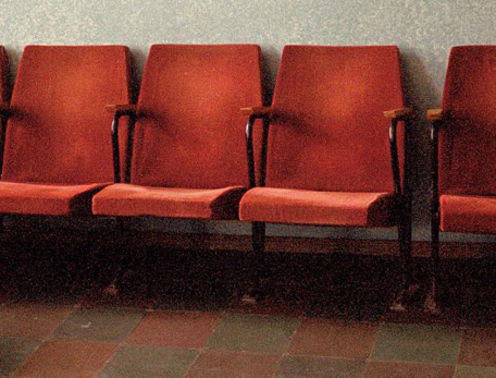 Person sitting on the floor, head down, empty chairs behind them