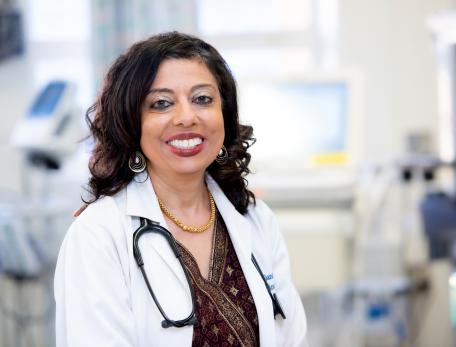 Monica Gandhi stands in a white coat, smiling at the camera