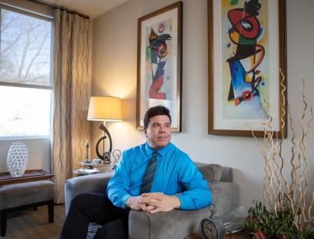 Roberto Olivardia sits in his office beneath two colorful paintings. 