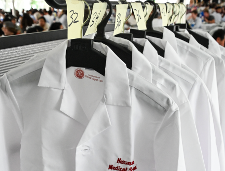 Several white coats embroidered with "Harvard Medical School" hanging on a hangers on a rack on white coat day