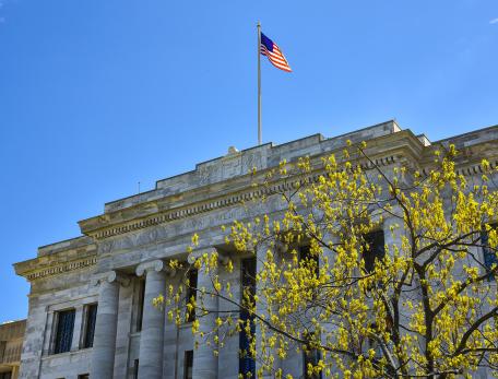 The American Flag flies over Harvard Medical School’s Gordon Hall, with new spring oak leaves on a tree in the foreground.