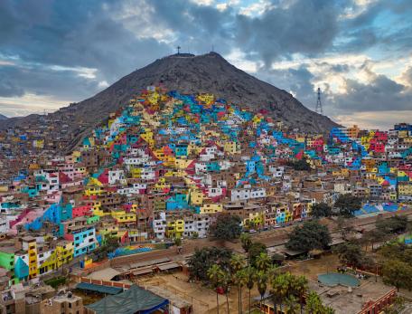 Aerial view of San Cristóbal Hill in the Rímac district of Lima, Peru, densely packed with informal housing and winding, narrow streets. The hillside is covered with colorful, tightly clustered homes built into the steep terrain, illustrating the crowded urban development of the area.