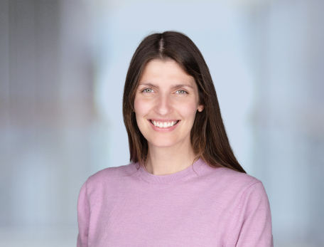 A headshot of a woman, Jennifer Oyler-Yaniv, in a pink shirt with straight brown hair, smiling at the camera