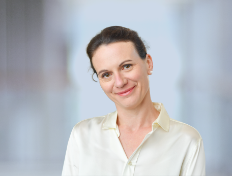 A woman with brown hair in a white button down shirt looks at the camera with a slight smile.