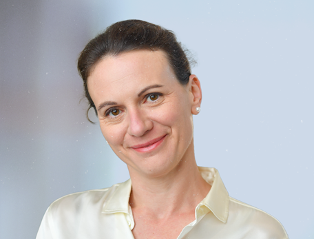 A woman with brown hair in a white button down shirt looks at the camera with a slight smile.