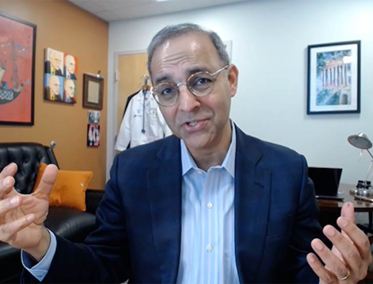 Jag Singh speaking to the camera in his office with a white coat hanging on the door