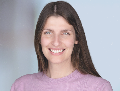A headshot of a woman, Jennifer Oyler-Yaniv, in a pink shirt with straight brown hair, smiling at the camera