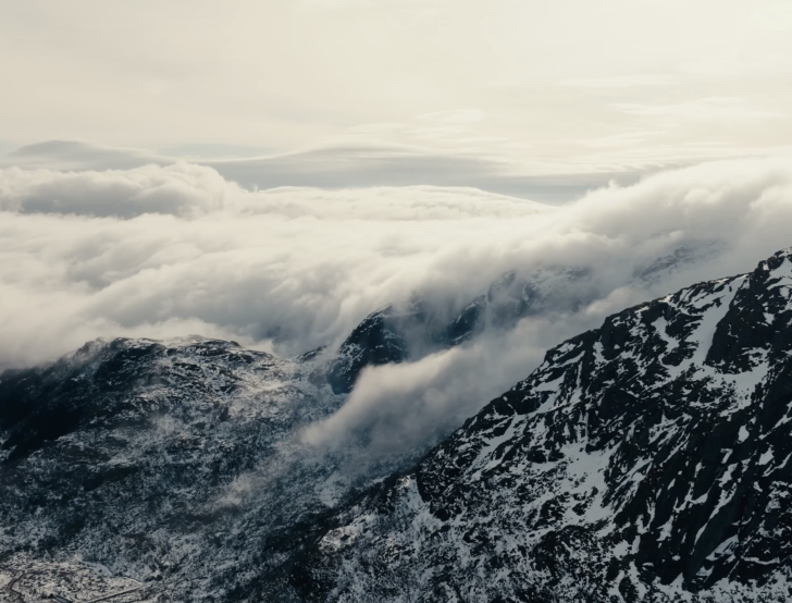 Clouds roll over a rocky mountain range as seen from high altitude.