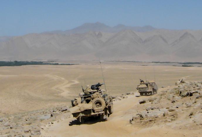 Military vehicles traveling over desert terrain with mountains in the distance