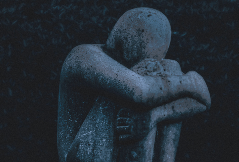 detail of a sculpture of a figure seated with knees pulled to chest