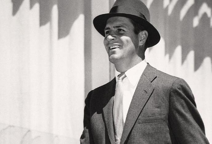black and white photo of a smiling suited man wearing a fedora