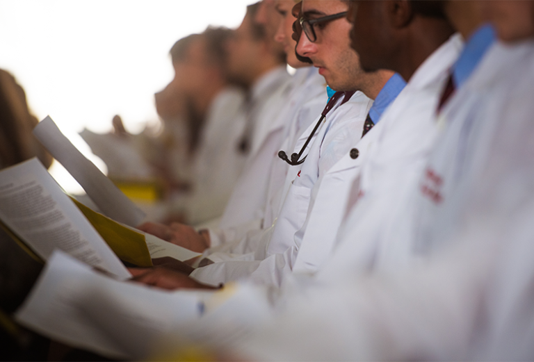 Students in white coats read paper documents