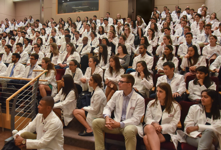 A group of students in white coats at a lecture