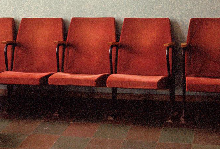 Person sitting on the floor, head down, empty chairs behind them