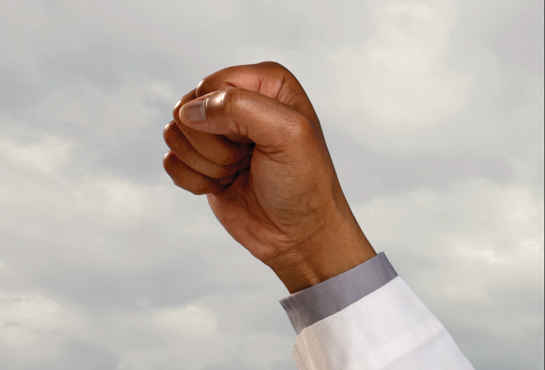 A raised fist of a Black man in a white coat