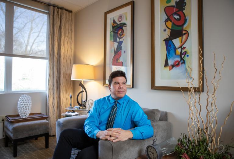 Roberto Olivardia sits in his office beneath two colorful paintings. 