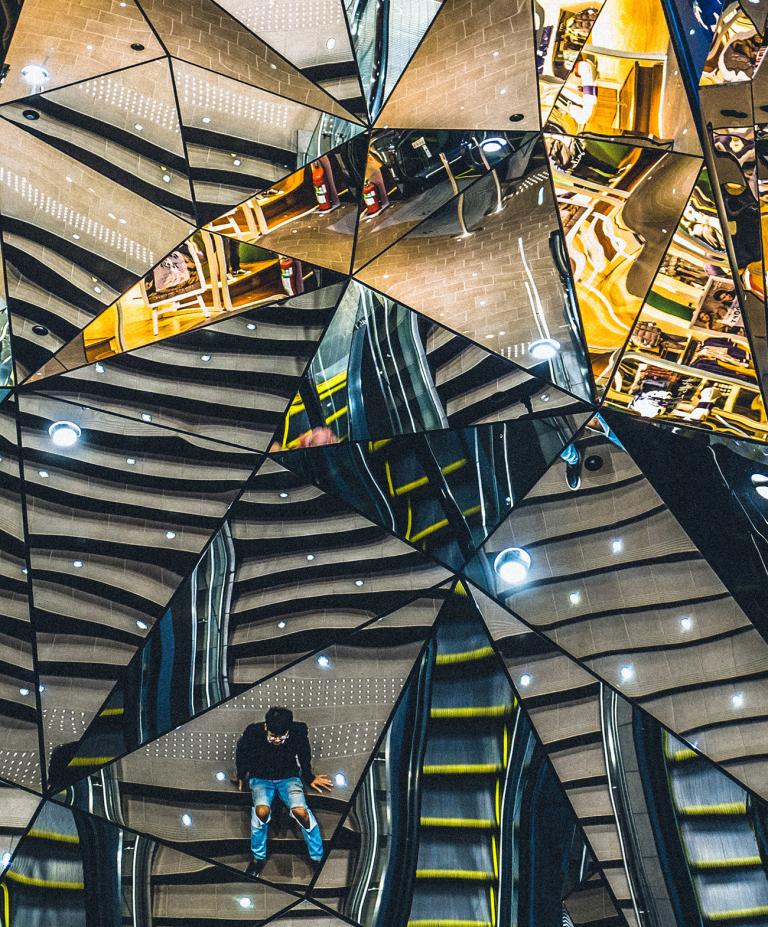 labyrinth of mirrors with reflections of various surfaces with single person seated in one section