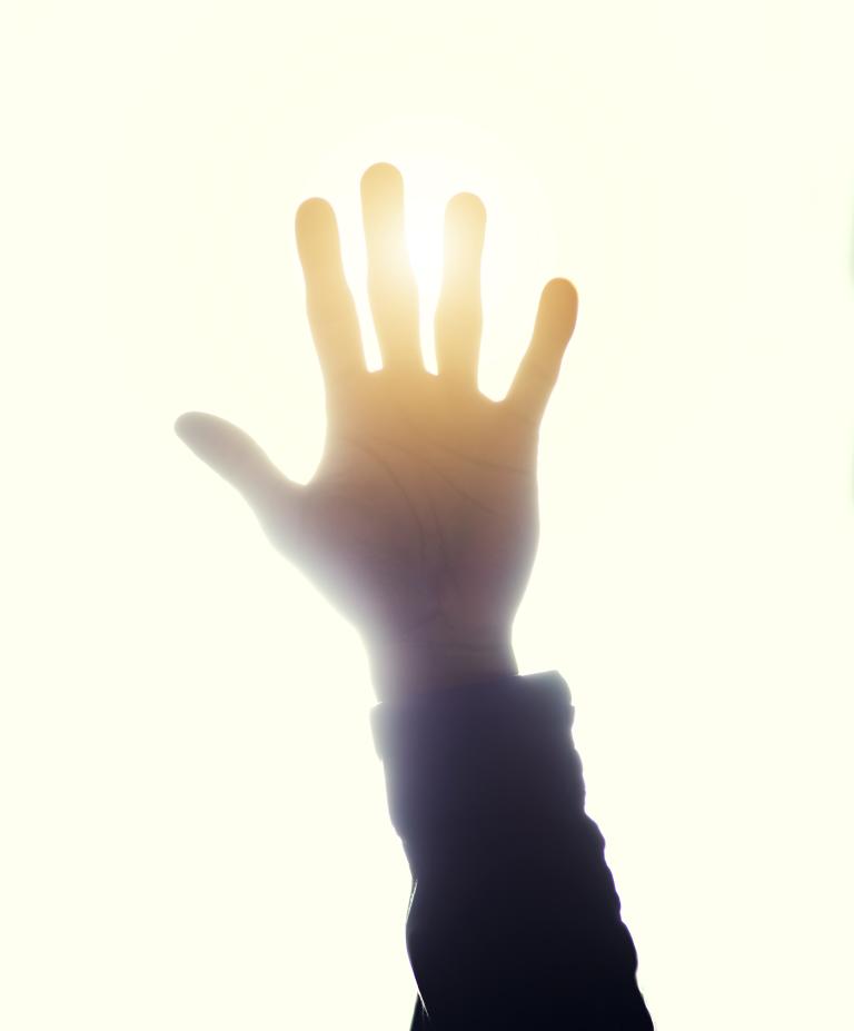 Looking up towards a hand that is blocking the sun