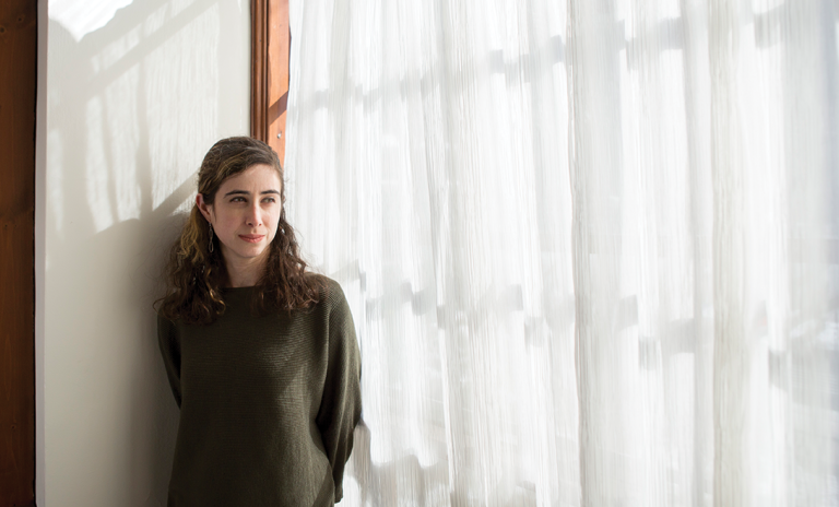 Lisa Rotenstein standing next to a window the light of which is being difused by a sheer curtain