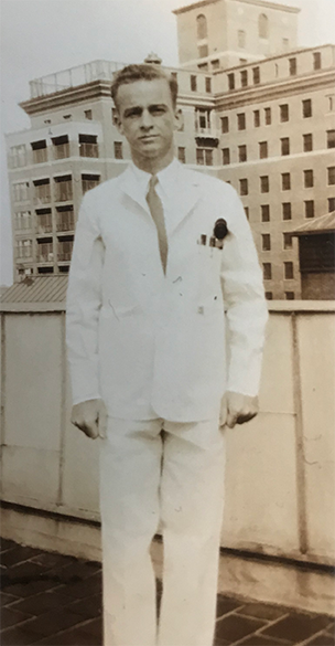 Perry Baird as a medical student, standing outdoors, wearing short white coat, pens in breast pocket