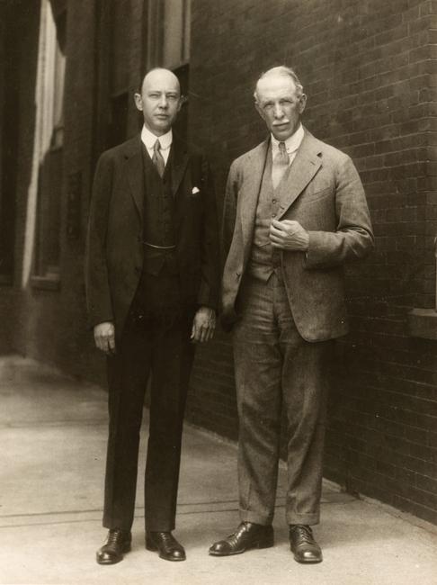 two men standing on a sidewalk in suits