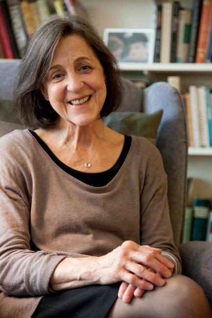 woman in a brown sweater sitting in a chair in front of a bookshelf