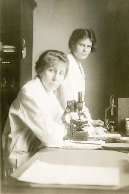 two women at a table with a microscope 