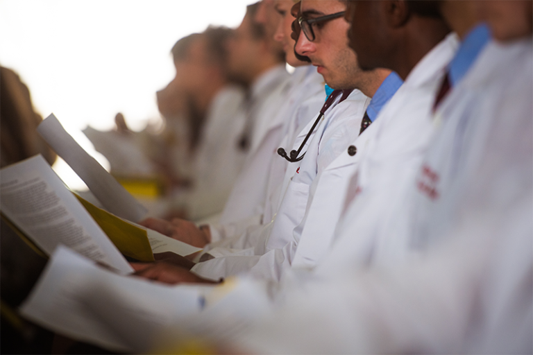 Students in white coats read paper documents