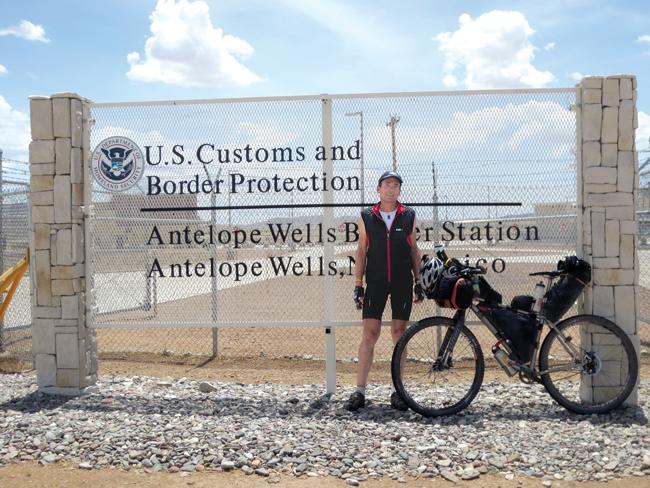 man standing next to his bike in front of a sign