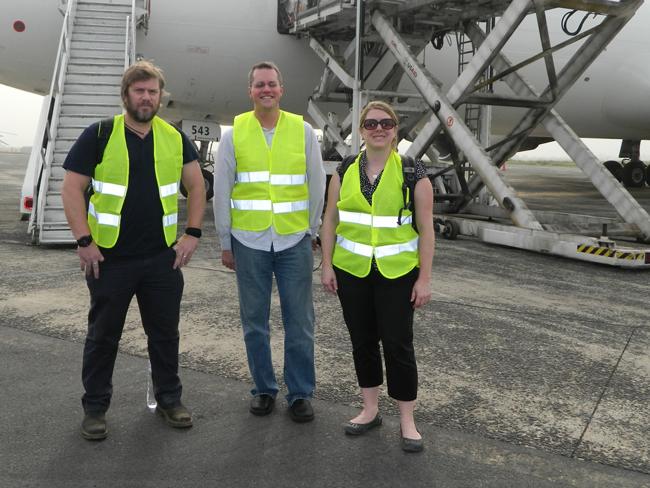 two men and a woman in yellow vests in front of an airplane 