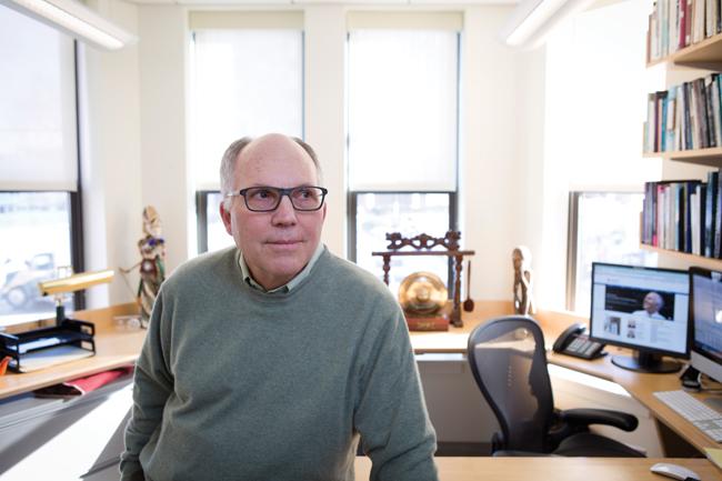 man in green sweater leaning on desk in his office