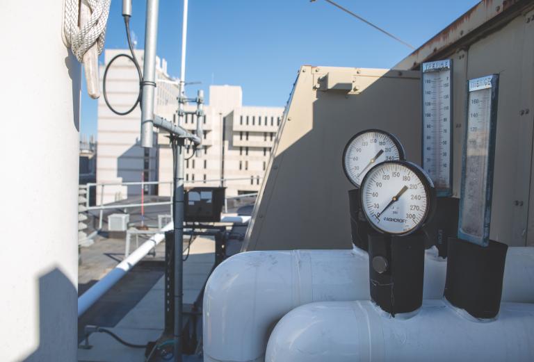 A close-up view of a pressure gauge on a white pipe on a rooftop