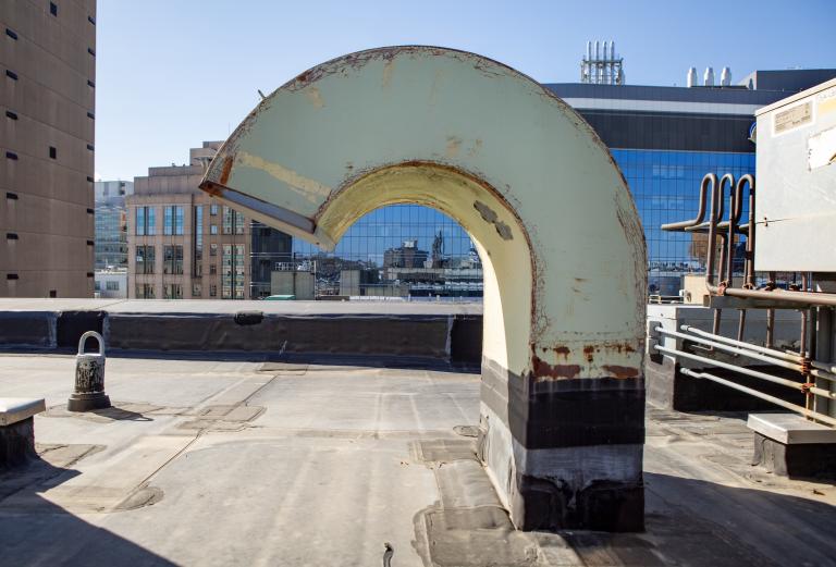 A rusty, pain-chipped vent emerges from the rooftop, curving to the left.