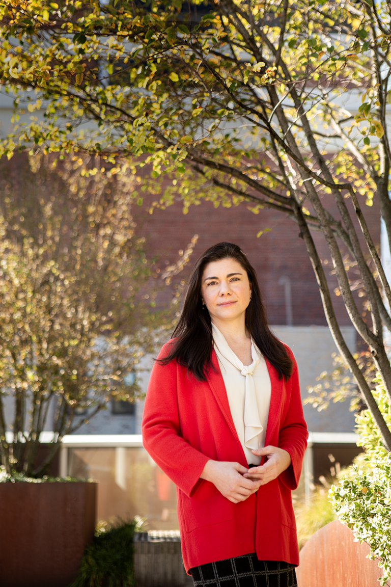 Antonia Seligowski stands outside a brick building with trees behind her. She has long brown hair and a bright red jacket.