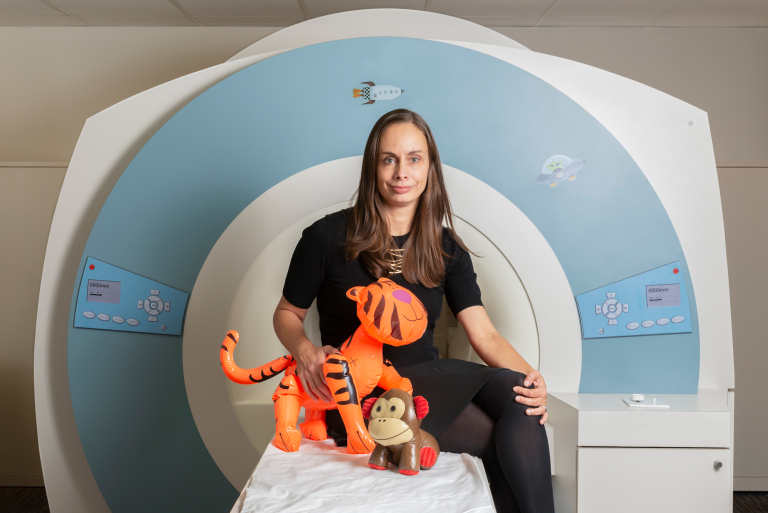 Nadine Gaab sits on the bed of an MRI machine holding two kids' toys, an inflatable tiger and monkey