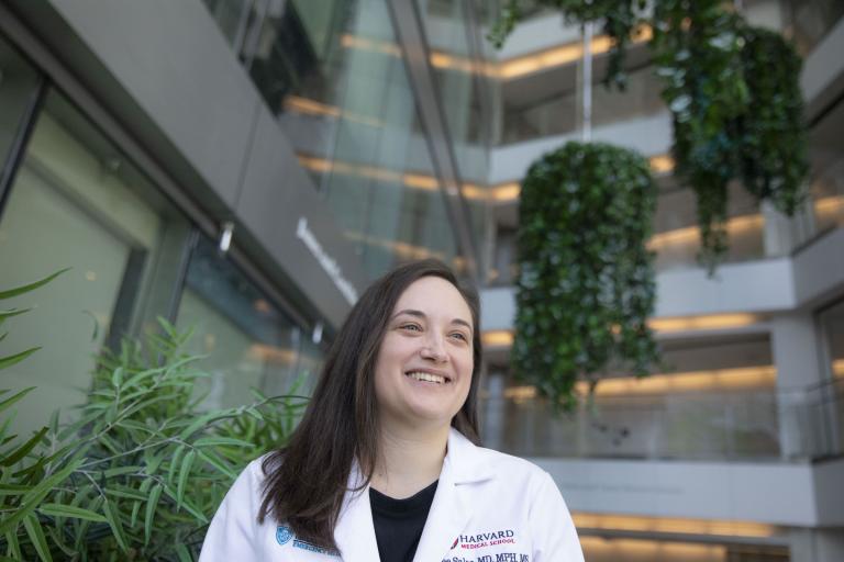 Renee Salas stands in the lobby of a building wearing a white coat and smiling.