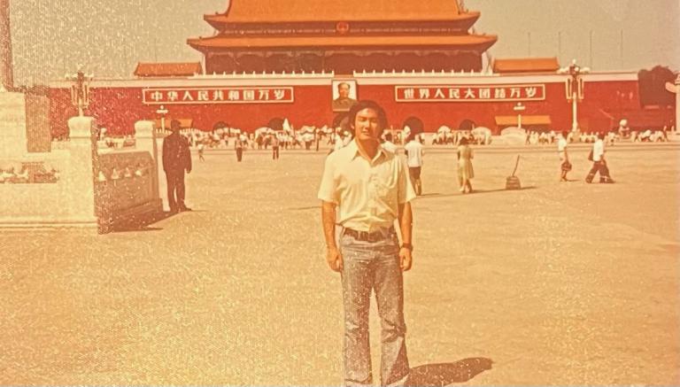 A man in a white shirt stands in Tiananmen Square in an old, sepia-toned photo