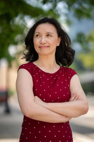 Wen Chen stands outside in a red dress with her arms crossed, looking to the left of the camera with a slight smile.