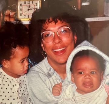 A vintage photo of a woman smiling at the camera wedged between two toddlers.