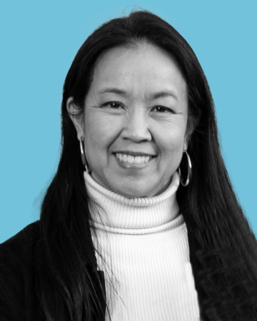 A headshot of a smiling woman with brown hair and a white turtleneck against a blue background. 