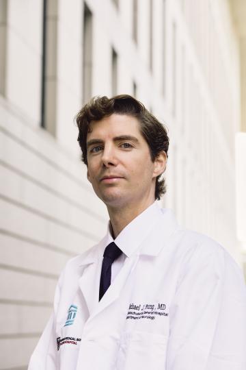 A man with brown hair and a white coat looks at the camera.